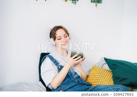 Woman with closed eyes listen music and enjoy cup of coffee or tea. Calm female spend free time at home enjoy favourite song with wireless modern headphones. Pastime weekend relax, no stress concept 109427691