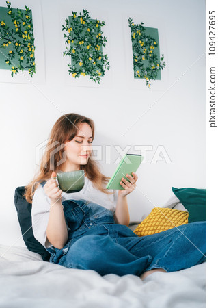 Young woman reading e-book on tablet reader in bed. Female relaxing with hot drink while reading an electronic book in cozy room. Mental health recovery, Personal growth. Hobby, Leisure time alone. Young woman reading e-book on tablet reader in bed. Female relaxing with hot drink while reading an electronic book in cozy room. Mental health recovery, Personal growth. Hobby, Leisure time alone. 109427695