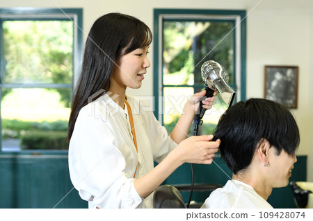 Female hairdresser drying a male customer's hair with a hair dryer 109428074
