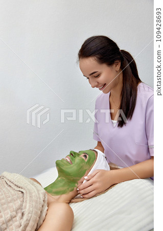 female beautician applies the mask to the face of beautiful woman in the spa salon. facial skin care 109428693