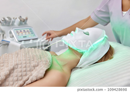 woman getting cosmetic procedure with LED facial mask in beauty salon woman getting cosmetic procedure with LED facial mask in beauty salon 109428698