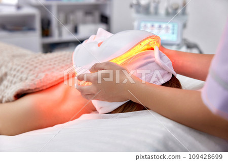 woman receiving led light anti-aging mask treatment from beautician in beauty salon woman receiving led light anti-aging mask treatment from beautician in beauty salon 109428699