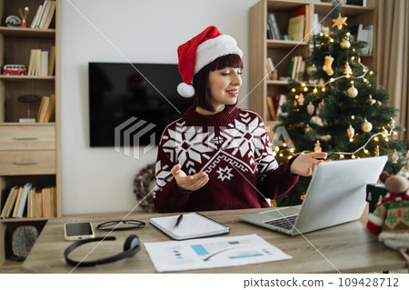 Female professional in Santa hat talking to client over video call on Christmas. Female professional in Santa hat talking to client over video call on Christmas. 109428712