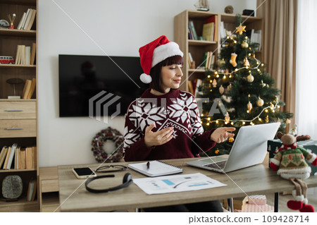 Female professional in Santa hat talking to client over video call on Christmas. Female professional in Santa hat talking to client over video call on Christmas. 109428714