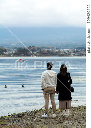Rear view of couple people holding hands of each other and looking at the lake view with landscape in background Rear view of couple people holding hands of each other and looking at the lake view with landscape in background 109429221