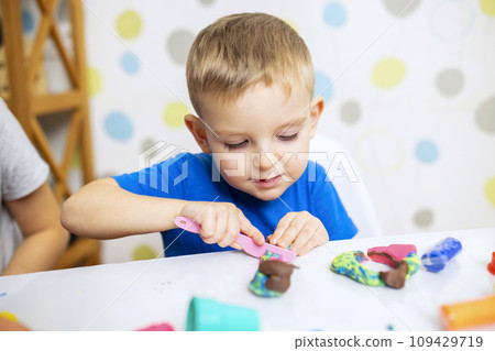 Little boy enthusiastically plays with plasticine, play dough on white table 109429719