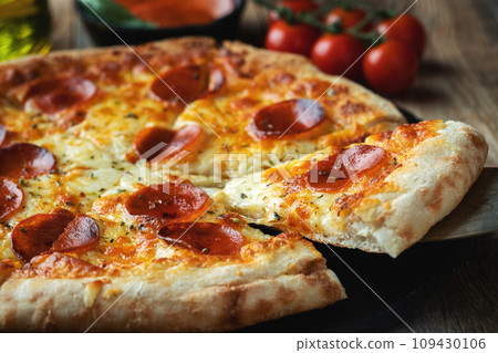 A slice of hot Italian pizza with stretching cheese. Pizza pepperoni on a dark wooden background A slice of hot Italian pizza with stretching cheese. Pizza pepperoni on a dark wooden background 109430106