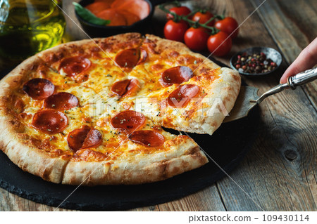 A slice of hot Italian pizza with stretching cheese. Pizza pepperoni on a dark wooden background A slice of hot Italian pizza with stretching cheese. Pizza pepperoni on a dark wooden background 109430114