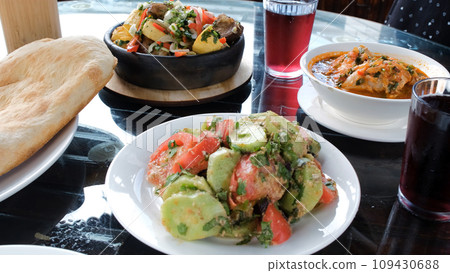 Close-up of various traditional tasty Georgian dishes on a table in cafe or a restaurant. Vegetable walnut sauce salad, ojahuri, chakhokhbili, freshly baked pitta bread and grape lemonade 109430688