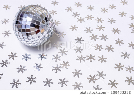 The disco ball lies on a white background strewn with silver snowflakes. New Year and Christmas background The disco ball lies on a white background strewn with silver snowflakes. New Year and Christmas background 109433238