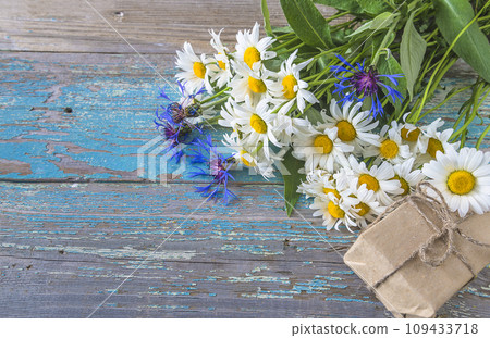 Bouquet of white daisies and bluecorns and handmade gift box on the old blue paint wooden background; space for text Bouquet of white daisies and bluecorns and handmade gift box on the old blue paint wooden background; space for text 109433718