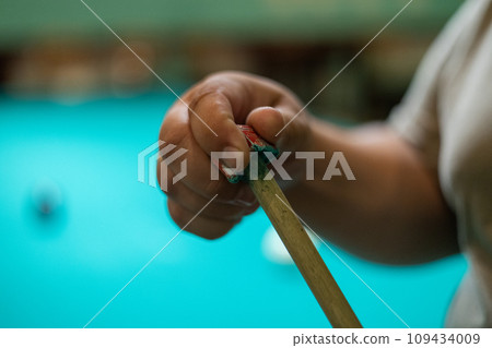 Close-up. A man's hand rubs the tip of a billiard cue with chalk for a more accurate shot. A man prepares to play billiards by rubbing his cue with chalk to prevent it from slipping. 109434009