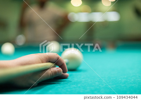 A man plays billiards effectively and hits the ball with a cue. A handsome man leans over a billiard table and makes a precise hit on a billiard ball. Concept of hitting the ball with a cue. A man plays billiards effectively and hits the ball with a cue. A handsome man leans over a billiard table and makes a precise hit on a billiard ball. Concept of hitting the ball with a cue. 109434044