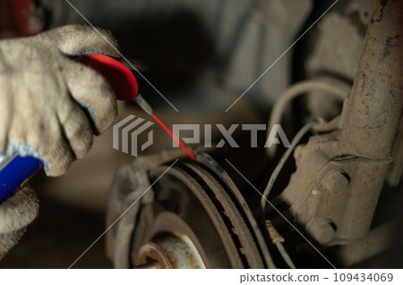 A man is repairing a car in a garage. A man treats rusted bolts with WD-40 solution. Replacing a brake disc on a car in the garage. Concept of a man fixing his car in a garage. A man is repairing a car in a garage. A man treats rusted bolts with WD-40 solution. Replacing a brake disc on a car in the garage. Concept of a man fixing his car in a garage. 109434069