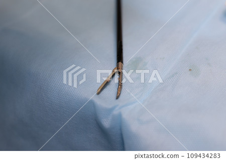 A sterile endoscopic clamp lies on the surgical table in the operating room, ready for use. Endoscopic tweezers on a blue surgical background. Endoscopic instrument concept. 109434283