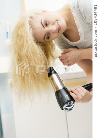 Blonde woman using hair dryer Blonde woman using hair dryer 109434491