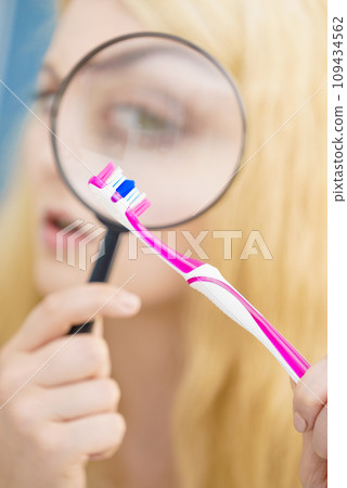 Woman looking at toothbrush through loupe 109434562