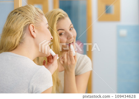 Woman in bathroom applying lip balm Woman in bathroom applying lip balm 109434628