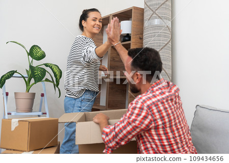 Positive man and woman highfive each other after successfully completing unpacking cardboard boxes with things in new apartment of residential complex friendly gesture and joy 109434656