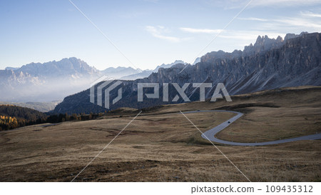 High mountain pass with curving road during early foggy morning, Dolomites, Italy 109435312