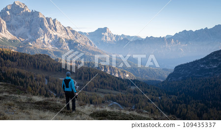 Man with camera enjoying views on beautiful mountain valley during early morning, Dolomites, Italy Man with camera enjoying views on beautiful mountain valley during early morning, Dolomites, Italy 109435337