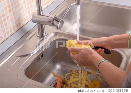 Female hands washing a peeling potato with hand under running water in sink in the kitchen 109435866