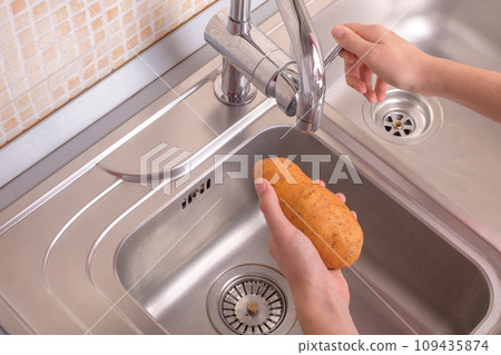 Female hands ready to washing potato in sink in kitchen Female hands ready to washing potato in sink in kitchen 109435874
