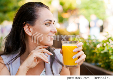 Happy business woman in street cafe drinks natural juice and smiles on sunny day. 109436139