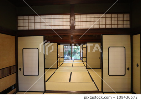 Scenery inside a house with tatami mats, sliding doors, transoms, and a Japanese-style room with a green garden visible beyond the window. Scenery inside a house with tatami mats, sliding doors, transoms, and a Japanese-style room with a green garden visible beyond the window. 109436572