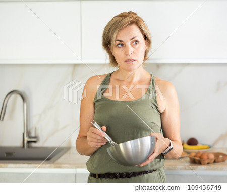 Middle-aged woman standing holding bowl in the kitchen 109436749