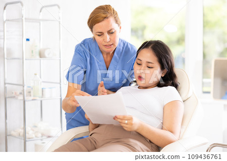 Friendly cosmetologist doctor offers girl patient to sign contract before the operation in beauty clinic Friendly cosmetologist doctor offers girl patient to sign contract before the operation in beauty clinic 109436761