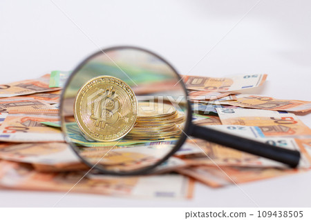 A Stack of Bitcoin Coins Visible Through a Magnifying Glass on the 50-Euro Banknotes A Stack of Bitcoin Coins Visible Through a Magnifying Glass on the 50-Euro Banknotes 109438505