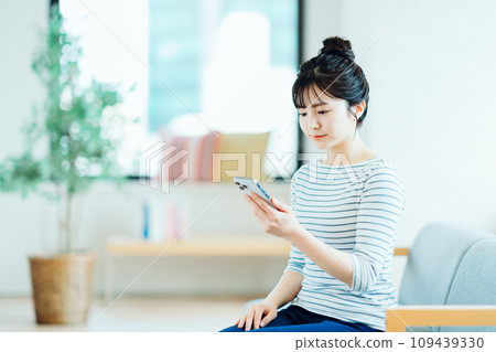 A young woman who operates a smartphone in the living room. A young woman who operates a smartphone in the living room. 109439330