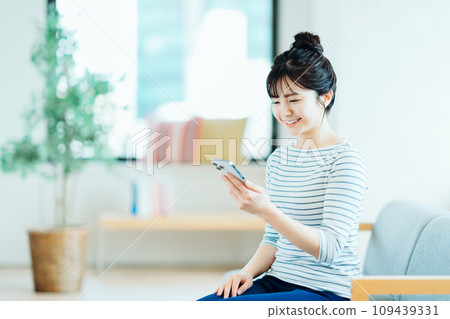 A young woman who operates a smartphone in the living room. A young woman who operates a smartphone in the living room. 109439331