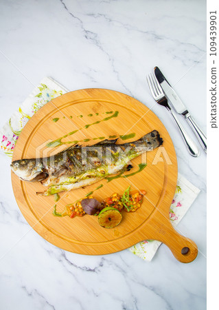 baked fish with lime and spices on a wooden tray on a marble background, top view 109439901