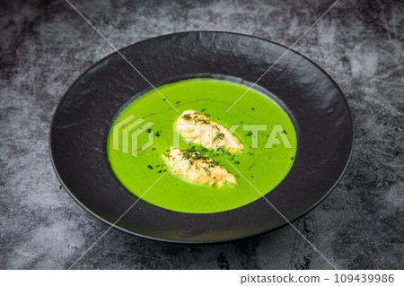 creamy broccoli soup with herbs in a black plate side view 109439986