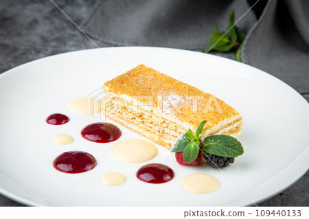 white sponge cake with drops of syrup, mint and wild berries on a round plate side veiw 109440133