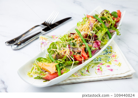 green salad with cherry tomatoes on a white oblong plate, side view 109440824