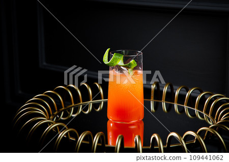 bright tropical cocktail with lime peel and gradient color in a transparent glass, side view 109441062