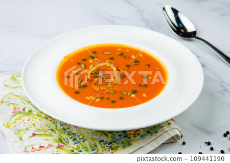 orange cream soup with pieces of meat in a white plate, side view 109441190