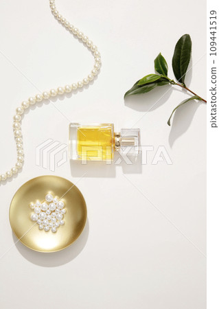 On a white background, a glass bottle container yellow liquid decorated with green leaves and pearl necklace. Minimal scene with mockup bottle for advertising perfume product. Top view On a white background, a glass bottle container yellow liquid decorated with green leaves and pearl necklace. Minimal scene with mockup bottle for advertising perfume product. Top view 109441519