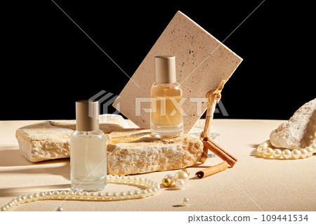 Creative background for advertising perfume product. Two glass bottles displayed with cinnamon stick, pearl necklace, stone and brick on black background. Mockup for design Creative background for advertising perfume product. Two glass bottles displayed with cinnamon stick, pearl necklace, stone and brick on black background. Mockup for design 109441534