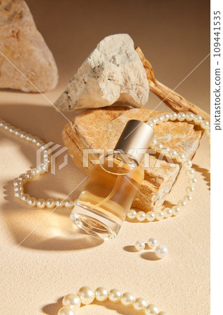 On a beige background with stone and pearl necklace, a glass perfume bottle unlabeled displayed. Minimal concept for advertising with mockup for design On a beige background with stone and pearl necklace, a glass perfume bottle unlabeled displayed. Minimal concept for advertising with mockup for design 109441535