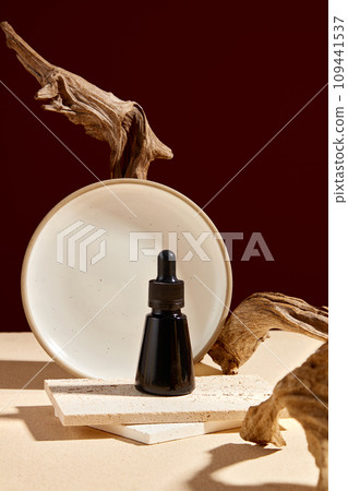 A black dropper bottle placed on brick podiums decorated with dry twigs and round dish on brown background. Front view, creative concept for advertising with minimal style A black dropper bottle placed on brick podiums decorated with dry twigs and round dish on brown background. Front view, creative concept for advertising with minimal style 109441537