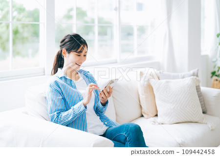 A woman sitting on a couch and operating a smartphone 109442458