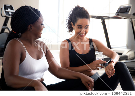 Two young woman talking in the gym, woman in sportswear and friend or coach relax and discussing. 109442531