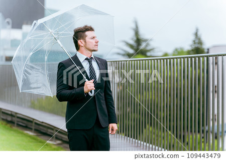 Foreign businessman holding a plastic umbrella during rainy season/typhoon rain 109443479