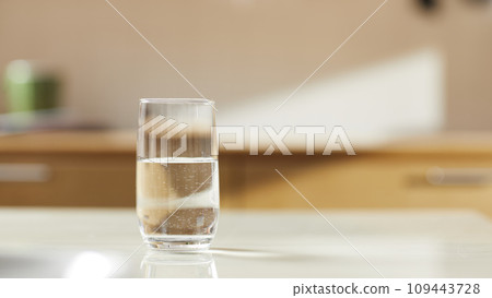 A sunny kitchen with white tile walls, a wooden table and sink. 109443728