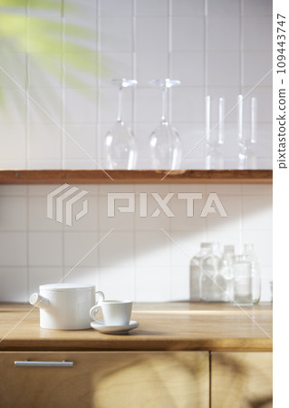 A sunny kitchen with white tile walls, a wooden table and sink. 109443747