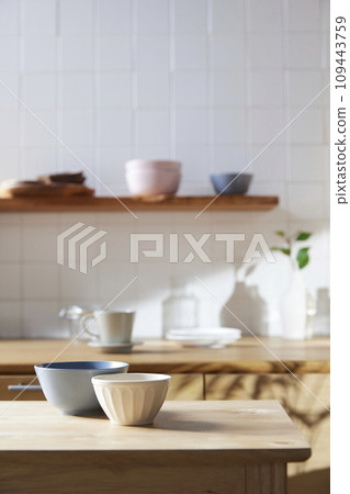 A sunny kitchen with white tile walls, a wooden table and sink. 109443759
